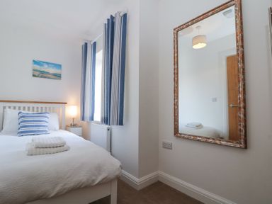 A bedroom with a bed with white bedding and blue striped cushion beside a window with blue and white striped curtains and a large mirror on the wall at Weydale Avenue in Scarborough