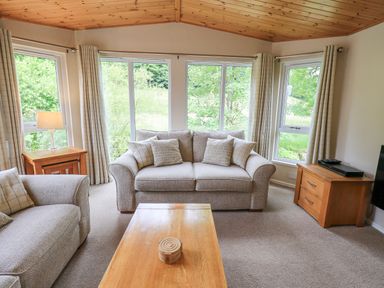 A living room with sofa armchairs wooden coffee table side tables and large windows at Esthwaite Lodge Beckside 43 Limefitt Park near Windermere