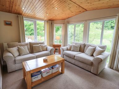 A living room with two sofas a wooden coffee table and large windows at Esthwaite Lodge in Beckside 43 Limefitt Park near Windermere