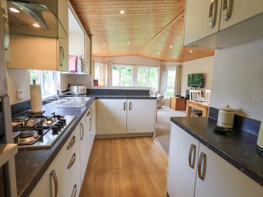 A kitchen with white cabinets and black countertops connected to a living area with dining table and chairs at Esthwaite Lodge Beckside 43 Limefitt Park near Windermere