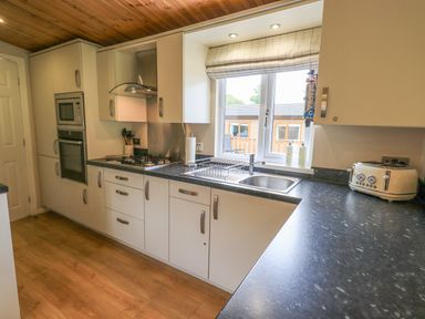 A kitchen with white cabinets black countertops a stainless steel sink and a window at Esthwaite Lodge Beckside 43 Limefitt Park near Windermere