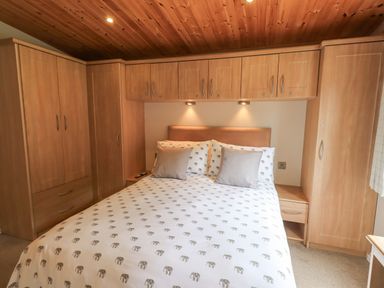 A bedroom with a double bed bedding with elephant prints and wooden wardrobes at Esthwaite Lodge Beckside 43 Limefitt Park near Windermere