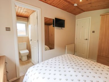 A bedroom with a bed, wardrobe, wall-mounted TV, radiator, and an en suite bathroom at Esthwaite Lodge Beckside 43 Limefitt Park near Windermere