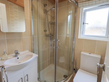 A bathroom with a corner shower enclosure a toilet and a sink with a mirror at Esthwaite Lodge Beckside 43 Limefitt Park near Windermere