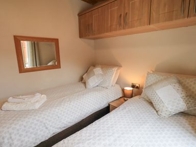 A bedroom with two single beds a bedside table with a lamp and wall cabinets at Esthwaite Lodge Beckside 43 Limefitt Park near Windermere