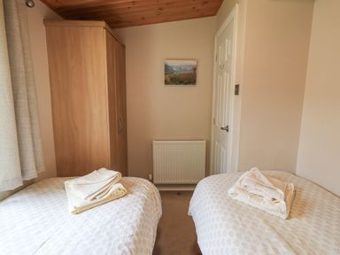 A bedroom with two single beds a wooden wardrobe a white door a radiator and a framed picture on the wall at Esthwaite Lodge Beckside 43 Limefitt Park near Windermere