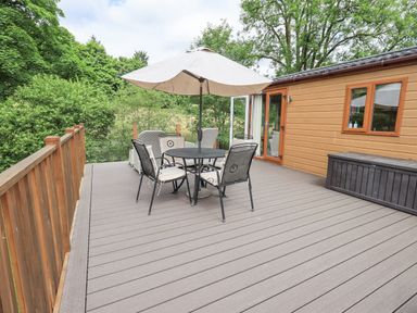 An outdoor deck with a table umbrella and chairs next to a wooden cabin at Esthwaite Lodge Beckside 43 Limefitt Park near Windermere
