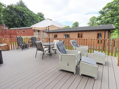 An outdoor deck with cushioned chairs a table with umbrella and wooden railing at Esthwaite Lodge Beckside 43 Limefitt Park near Windermere