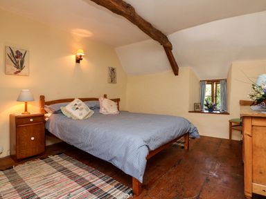 A bedroom with a bed and two pillows a wooden nightstand with a lamp and a wooden dresser by a small window at Bell Buoy Cottage in Morwenstow
