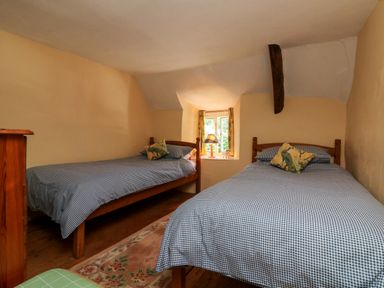 A bedroom with two single beds with checkered bedding and a window with a lamp at Bell Buoy Cottage in Morwenstow