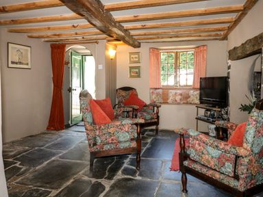 A living room with floral armchairs red cushions stone floor and a television at Bell Buoy Cottage in Morwenstow