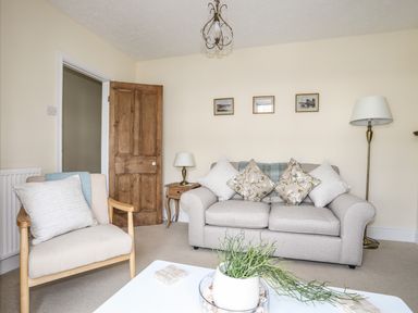 A living room with a sofa with cushions an armchair a wooden door and a coffee table with a plant at Hyfrydle in Borth-Y-Gest