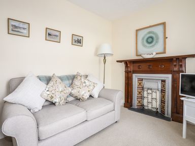 A living room with a beige sofa with cushions next to a wooden fireplace and a floor lamp at Hyfrydle in Borth-Y-Gest