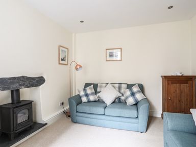 A living room with a blue sofa cushions a wood burning stove and a wooden cabinet at Hyfrydle in Borth-Y-Gest