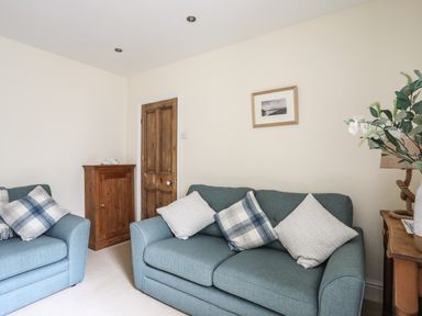 A living room with blue sofas cushions wooden cabinet and framed picture at Hyfrydle in Borth-Y-Gest