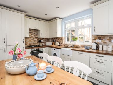 A kitchen with white cabinets wooden countertops a wooden table with tea set and flowers at Hyfrydle in Borth-Y-Gest