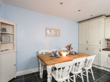 A kitchen dining area with a wooden table white chairs a candle flowers and kitchen cabinets at Hyfrydle in Borth-Y-Gest