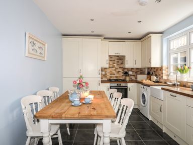 A kitchen with white cabinets wooden countertops and a wooden dining table with white chairs at Hyfrydle in Borth-Y-Gest