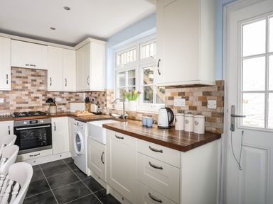 A kitchen with white cabinets wooden countertops tiled backsplash and appliances at Hyfrydle in Borth-Y-Gest