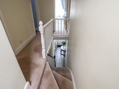 A stairway with beige carpeting and a white wooden banister leading to a hallway with a tiled floor and a table with flowers at Hyfrydle in Borth-Y-Gest