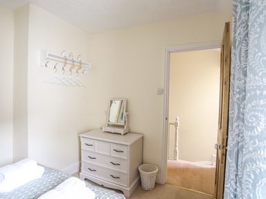 A bedroom corner with a white dresser topped with a small mirror a wall-mounted coat rack with hangers and an open door showing a hallway at Hyfrydle in Borth-Y-Gest