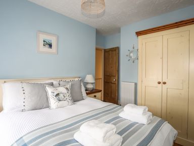 A bedroom with a bed, pillows, bedside table with lamp, wardrobe, and a door at Hyfrydle in Borth-Y-Gest