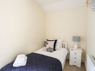 A small bedroom with a single bed a white nightstand and a lamp at Hyfrydle in Borth-Y-Gest