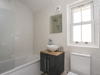 A bathroom with a bathtub a sink on a wooden countertop below a mirror and a toilet beside a window at Hyfrydle in Borth-Y-Gest