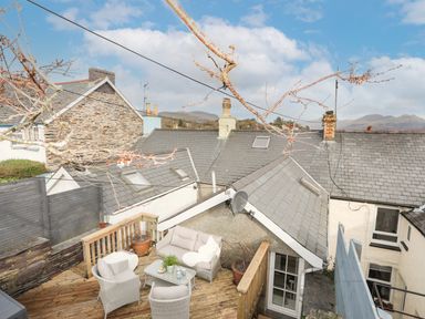 An outdoor wooden deck with wicker seating and a table surrounded by rooftops at Hyfrydle in Borth-Y-Gest