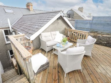 An outdoor wooden deck with white wicker furniture a glass table with a tea set and plants at Hyfrydle in Borth-Y-Gest