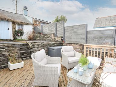 An outdoor patio with wicker chairs and a table with cups and a teapot at Hyfrydle in Borth-Y-Gest