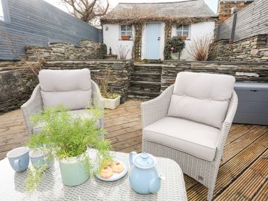 An outdoor seating area with two cushioned chairs a table with a teapot cups cookies and a plant stone steps leading to a small white building with a blue door at Hyfrydle in Borth-Y-Gest