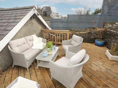An outdoor seating area with wicker furniture including a sofa and chairs on a wooden deck at Hyfrydle in Borth-Y-Gest