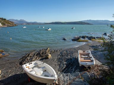Two small boats on rocky shoreline with water and hills in the background at Hyfrydle in Borth-Y-Gest