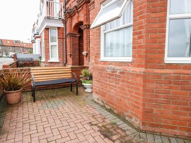 A small paved front yard with a wooden bench and potted plants outside a red brick house at Ellan Vannin in Sheringham