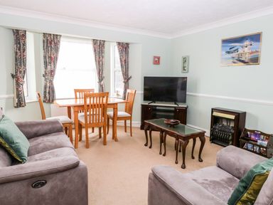 A living room with a dining table and chairs a television on a stand and two sofas at Ellan Vannin in Sheringham