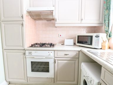 A kitchen with white cabinets gas stove oven microwave toaster and washing machine at Ellan Vannin in Sheringham