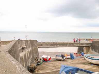 Small boats on a wooden slipway next to a concrete sea wall with people walking on a bridge above by the sea at Ellan Vannin in Sheringham