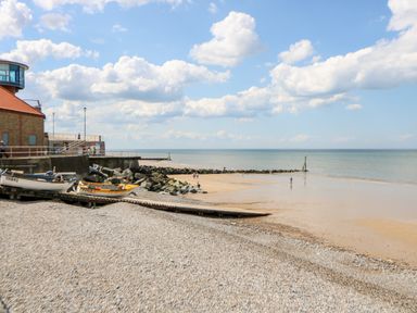 A pebble beach with boats on a ramp and a sandy shoreline with people near the sea at Ellan Vannin in Sheringham