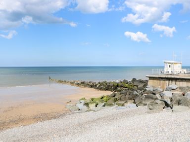 A sandy beach with rocks and a small building on a pier by the sea at Ellan Vannin in Sheringham