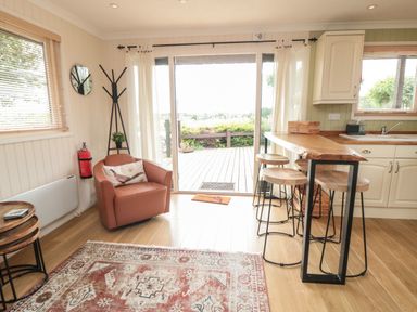 A living area with a leather chair a wooden high table with stools a rug and sliding glass doors at 3 Valley View Lodges Nawton near Helmsley