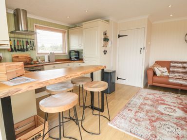 A kitchen and living area with a wooden countertop and stools a brown sofa and a patterned rug at 3 Valley View Lodges Nawton near Helmsley