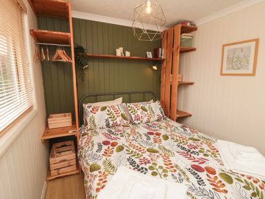 A bedroom with a bed with floral bedding wooden shelves hanging space and a framed picture on the wall at 3 Valley View Lodges Nawton near Helmsley