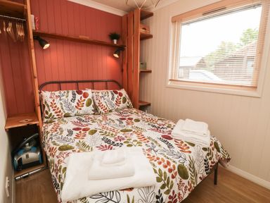 A bedroom with a bed with patterned bedding two wall lamps a window and wooden shelves at 3 Valley View Lodges Nawton near Helmsley