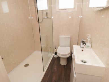 A bathroom with a shower area with glass divider a toilet and a sink with a faucet and soap dispenser at 3 Valley View Lodges Nawton near Helmsley