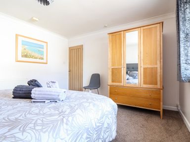 A bedroom with a bed having folded towels on it a wooden wardrobe with a mirror a gray chair a door and a framed picture on the wall at Summerhayes in Park Bottom