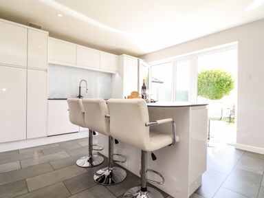 A modern kitchen with a white island and three white bar stools at Summerhayes in Park Bottom