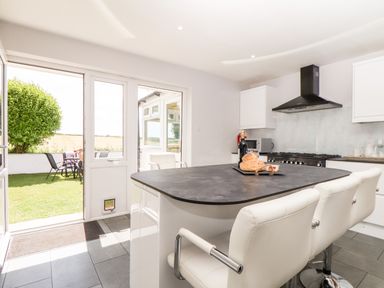 A kitchen with a black countertop island and white chairs next to a door leading to a garden at Summerhayes in Park Bottom