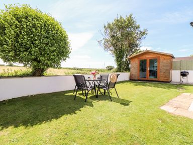 A garden with a round table and chairs on grass and a wooden shed in the background at Summerhayes Park Bottom