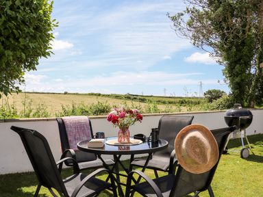 An outdoor patio area with a round glass table and four black chairs a vase with flowers on the table and a barbecue grill on the grass at Summerhayes in Park Bottom